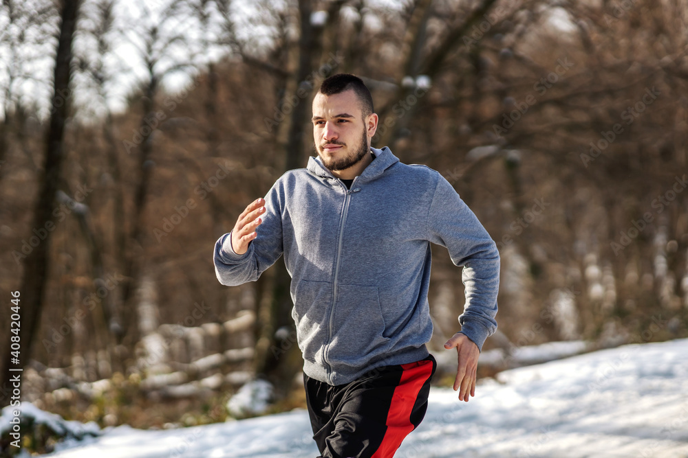 Sportsman running on snowy path in nature at sunny winter day. Winter fitness, cardio exercises, healthy habits Sportsman running on snowy path in nature at sunny winter day. Winter fitness, cardio exercises, healthy habits