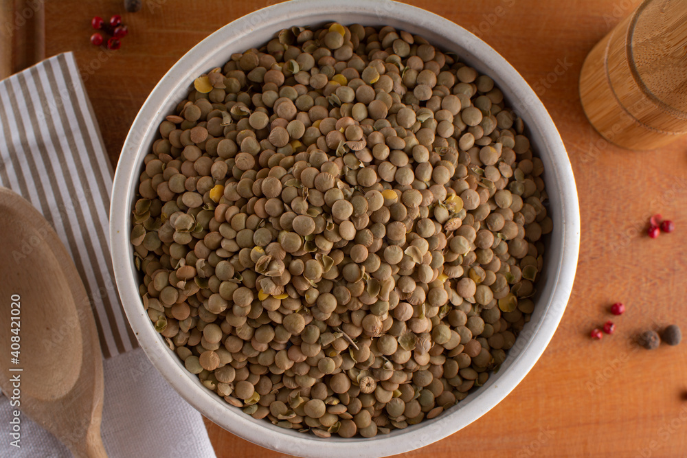Lentils and spoon in a white bowl close up on an old table.