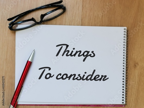 Top view text Things to consider on note book with pen and eye glasses on wooden table.