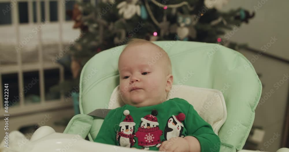 Beautiful look of christmas toddler in kid chair during feeding with spoon Beautiful look of christmas toddler in kid chair during feeding with spoon