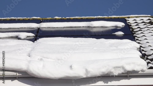 Melt water dripping from a rooftop in the early Spring. The snow reveals solar panels