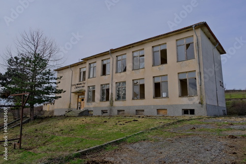 07.01.2021. Bulgaria, Kardzali. Old brownfield and abandoned soviet type school with overcast and very cloudy sky. School inside the green grass with broken windows. © SKahraman