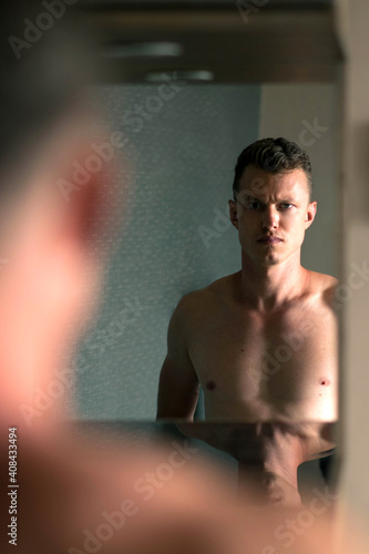 Young handsome man looking to mirror at home bathroom