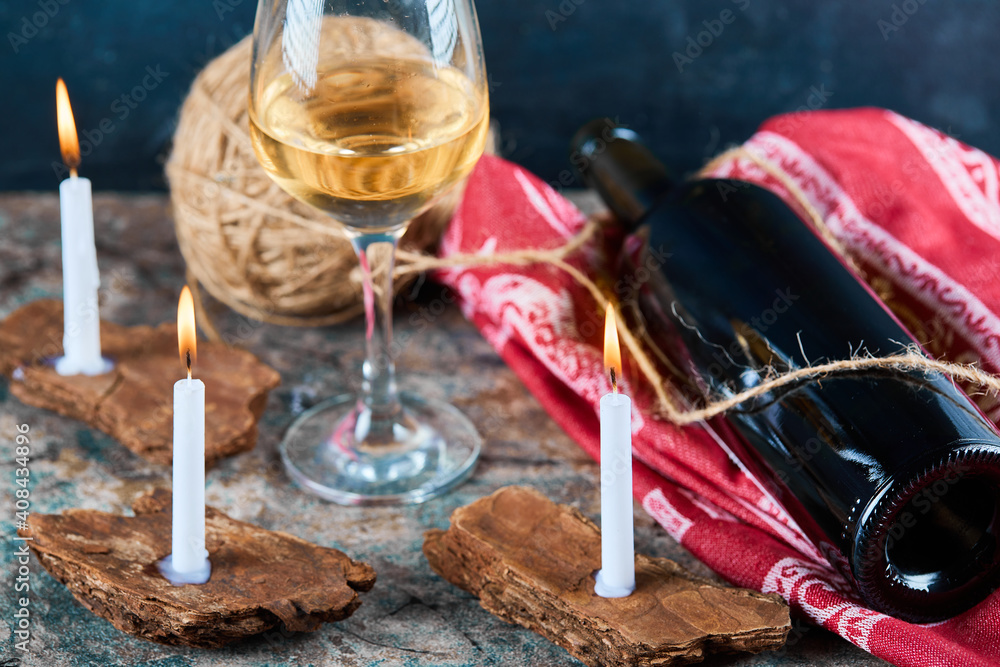 A glass of white wine and bottle with burning candles, close up