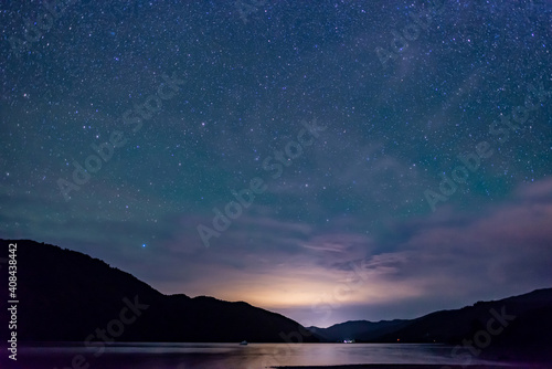 starry sky above the shape of mountains with the light of a city in a fjord in the Marlborough Sounds  New Zealand