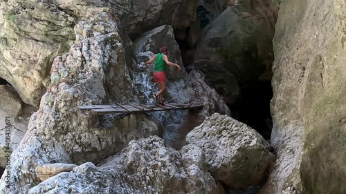 Slow motion of woman that crosses a little wooden bridge between rocks photo