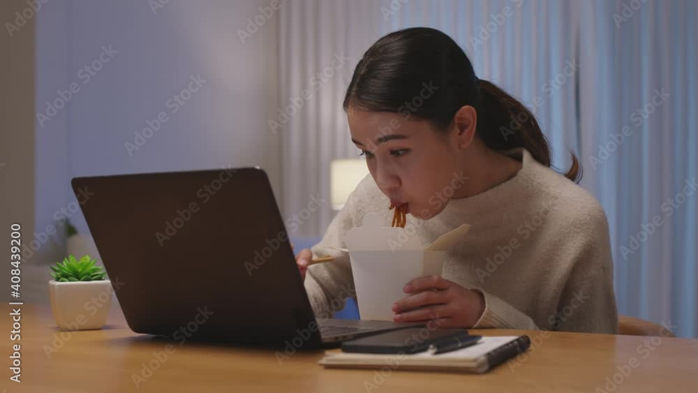 Young attractive beautiful asian female hungry eat instant noodles chinese food box take away full mouth look at computer notebook at home in busy work from home late night multitask unhealthy meal. Young attractive beautiful asian female hungry eat instant noodles chinese food box take away full mouth look at computer notebook at home in busy work from home late night multitask unhealthy meal.