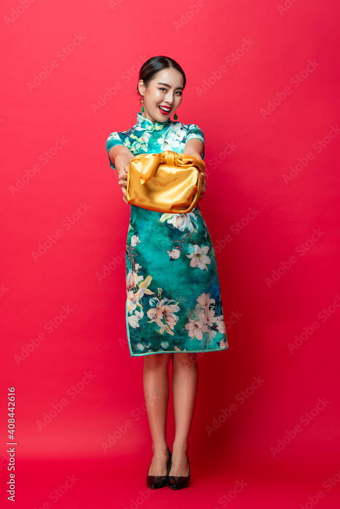 Happy smiling Asian woman in traditional costume giving gold gift box in red isolated studio background for Lunar new year concepts Happy smiling Asian woman in traditional costume giving gold gift box in red isolated studio background for Lunar new year concepts