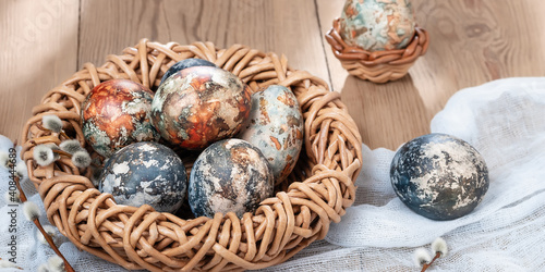 Easter composition - Easter eggs painted with natural dyes in a wicker nest on a wooden table