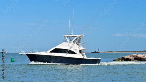 Broadside view of a beautiful white and black fishing yacht boat sails past breakwater on the calm blue water on a sunny day.