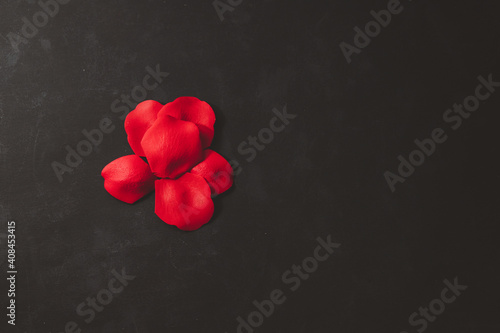 A pile of bright red rose petals in a heart shape placed on a black background, Valentine's Day concept, Christmas Day.