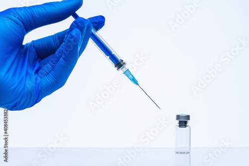 The coronavirus vaccine and syringe injection in the hand in a medical glove. Vial with vaccine against coronavirus. The concept of protection against coronavirus infection, COVID-19
