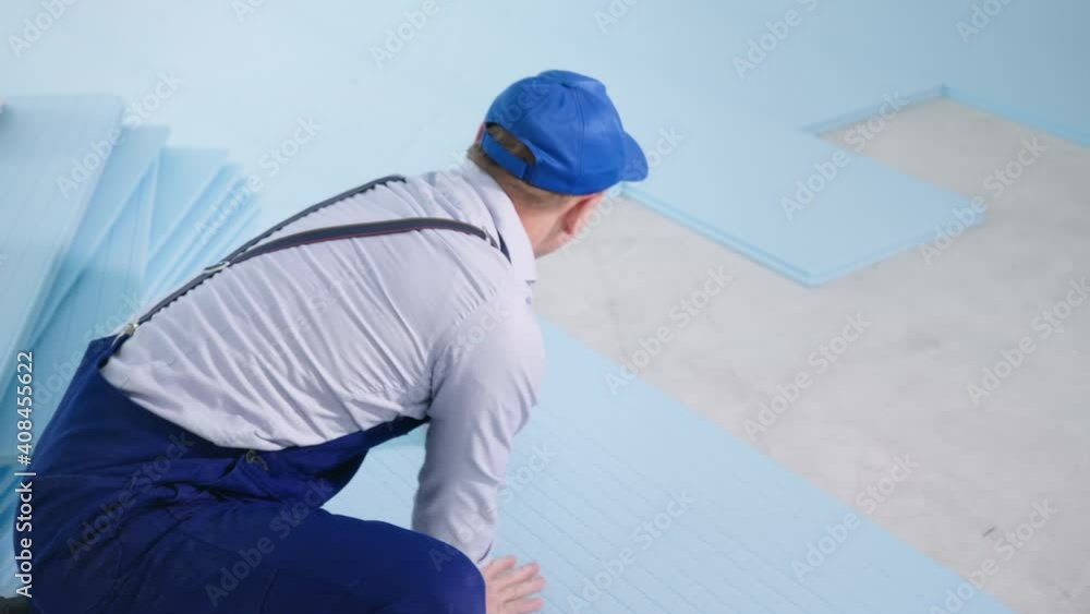 male construction company employee in special clothing lays polystyrene foam for insulation and laminate flooring indoors during renovations male construction company employee in special clothing lays polystyrene foam for insulation and laminate flooring indoors during renovations