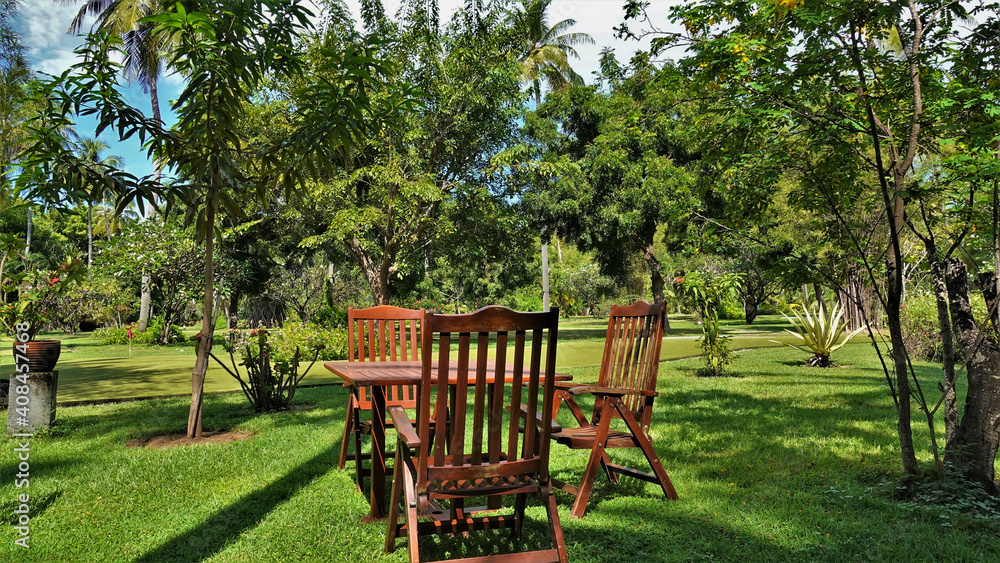 The garden lawn has a wooden table and chairs. Tropical vegetation grows around. Relaxing on a sunny summer day. Maldives
