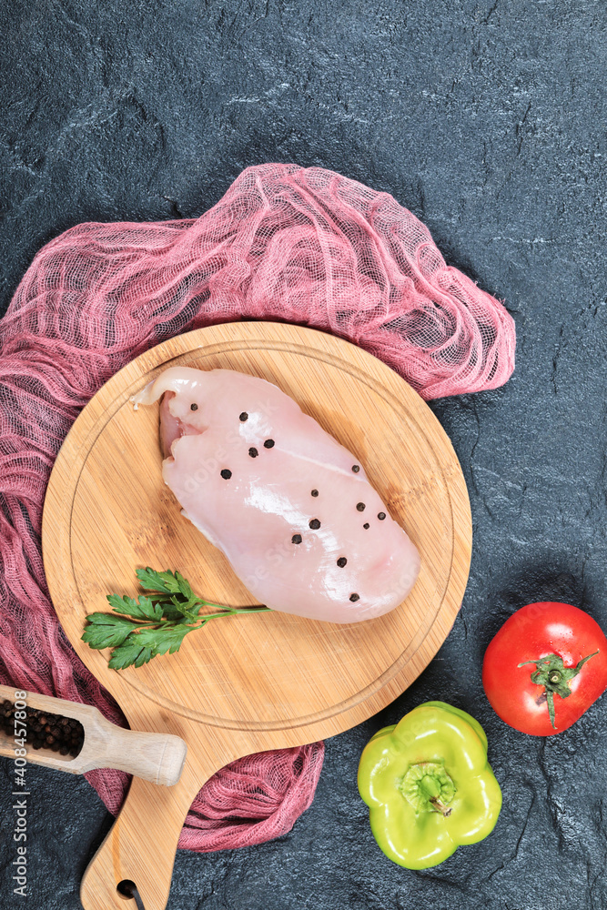 Raw chicken fillet on wooden board with vegetables and tablecloth