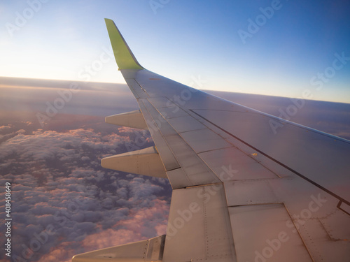 夜明けの飛行場を離陸し、朝日を浴びて飛行する飛行機に搭乗して窓から撮影した翼