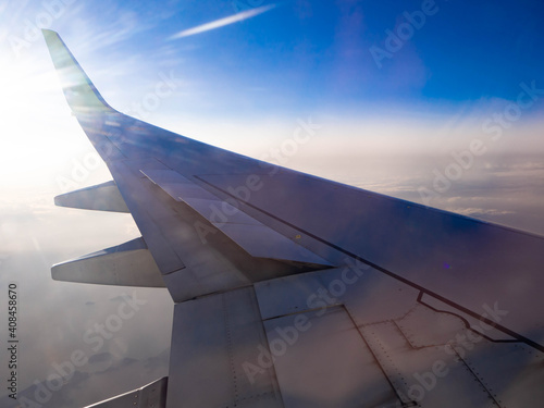 夜明けの飛行場を離陸し、朝日を浴びて飛行する飛行機に搭乗して窓から撮影した翼
