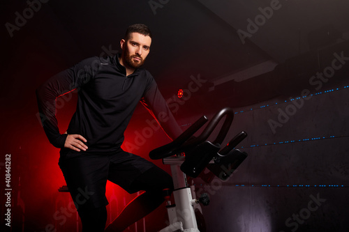 male sitting on bike in gym posing at camera, workout ride a bike in gym, with the intention of healthcare. red neon smoky space in the background