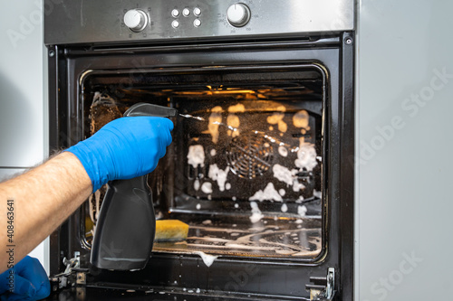 a man washes the oven with foam and a spray bottle. House cleaning