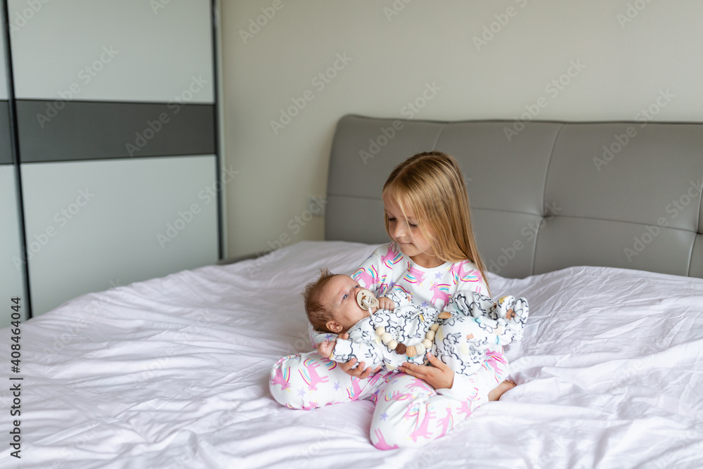 Little sister and her baby brother. Toddler kid playing with new sibling. Girl and baby 2-3 months old relax in a home bedroom. Family with two children at home. Love, trust and tenderness concept Little sister and her baby brother. Toddler kid playing with new sibling. Girl and baby 2-3 months old relax in a home bedroom. Family with two children at home. Love, trust and tenderness concept