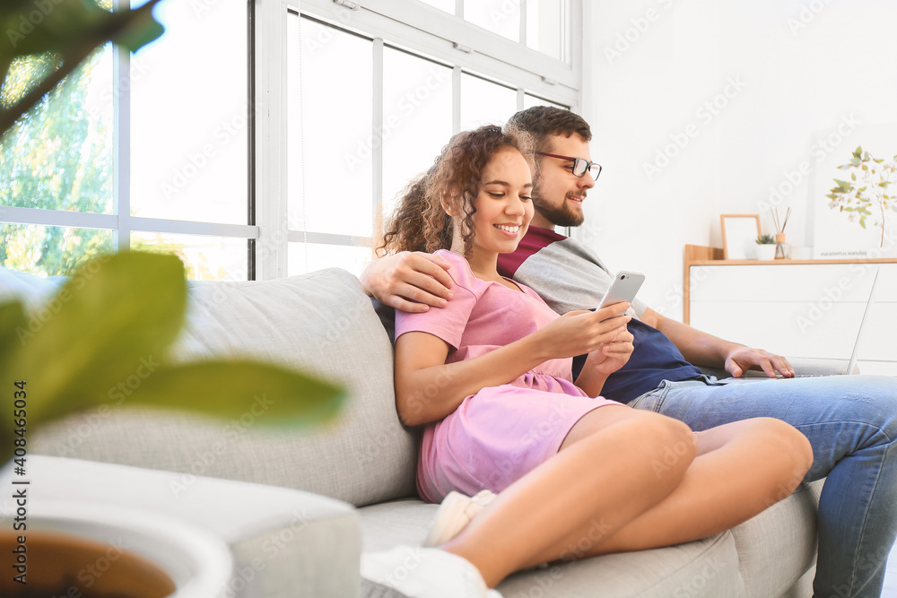 Young couple with gadgets relaxing on sofa at home Young couple with gadgets relaxing on sofa at home