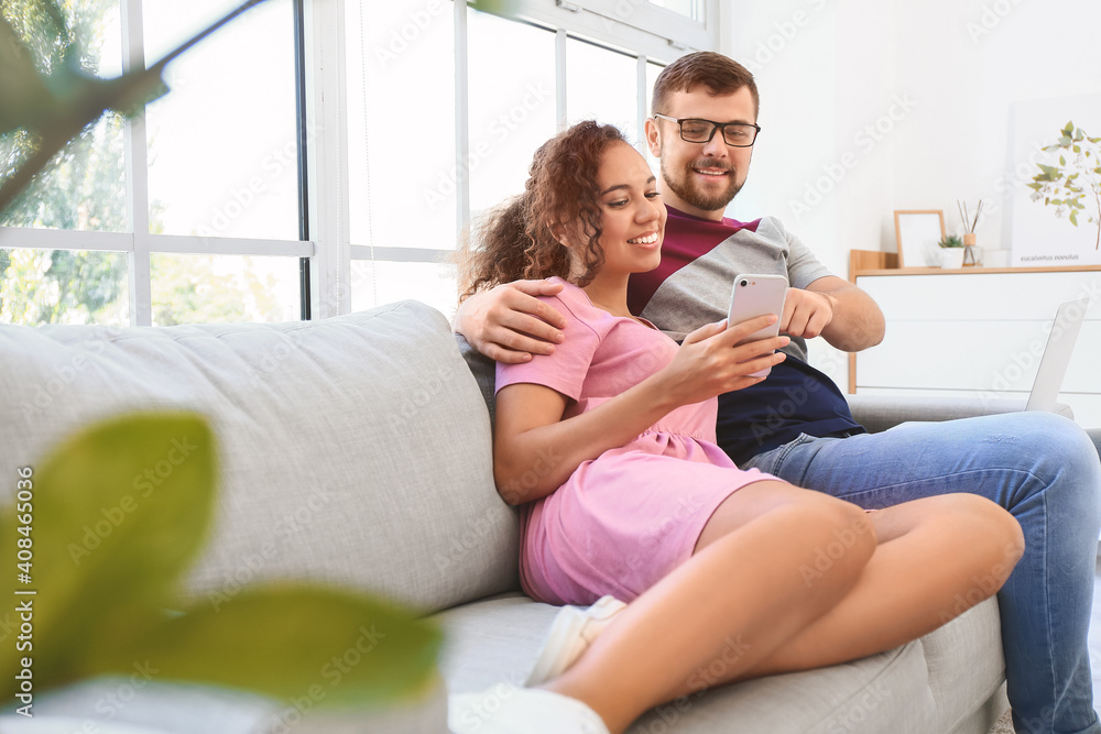 Young couple with mobile phone relaxing on sofa at home