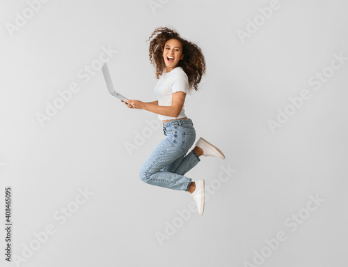 Tela Young woman with laptop jumping on light background