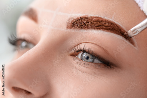 Young woman undergoing eyebrow correction procedure in beauty salon, closeup photo