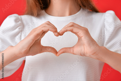 Young woman making heart with her hands on color background, closeup photo