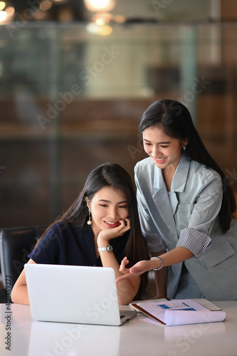 Happy friendly employee talking to her colleague teammate sharing ideas chatting at office.