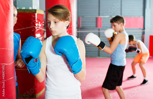 Adult boxing instructor and cheerful children practicing blows on boxing bag