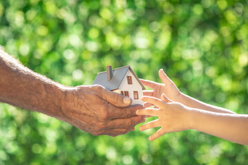 Family holding eco house in hands against spring green background