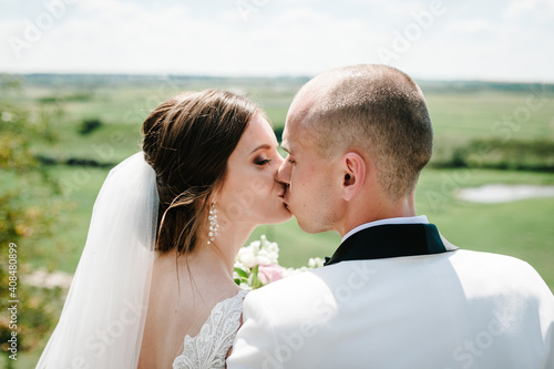Bride and groom kissing and holding bouquet of flowers on nature. Romantic couple newlyweds outdoors. Wedding ceremony. © Serhii