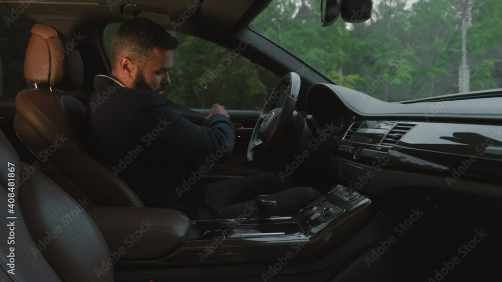 Medium shot of brutal mixed-race businessman in suit getting in drivers sear of posh car and fastening seatbelt Medium shot of brutal mixed-race businessman in suit getting in drivers sear of posh car and fastening seatbelt