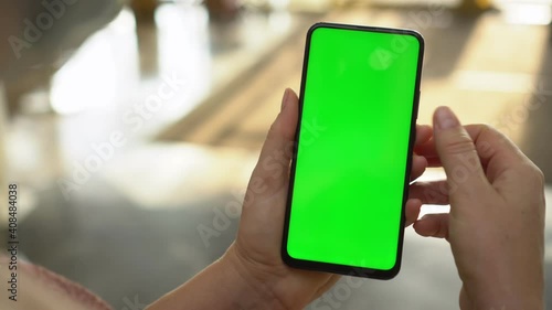 Back view of brunette holding chroma key green screen smartphone watching content.Shopping center. Department store. Mall. Shopping online. Gadgets and contemporary people concept.