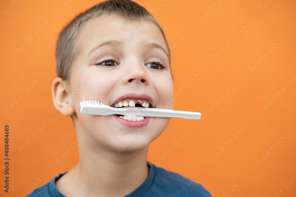 Boy without milk upper tooth in blue t-shirt holds toothbrush in his mouth on the orange background. Boy without milk upper tooth in blue t-shirt holds toothbrush in his mouth on the orange background.