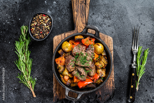 Meat stew in cooking pot on dark rustic cutting board. Black background. Top view