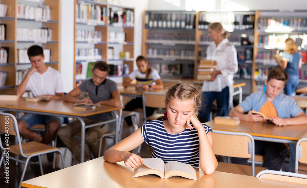 Obraz premium Schoolgirl preparing for lesson in school library, reading textbooks