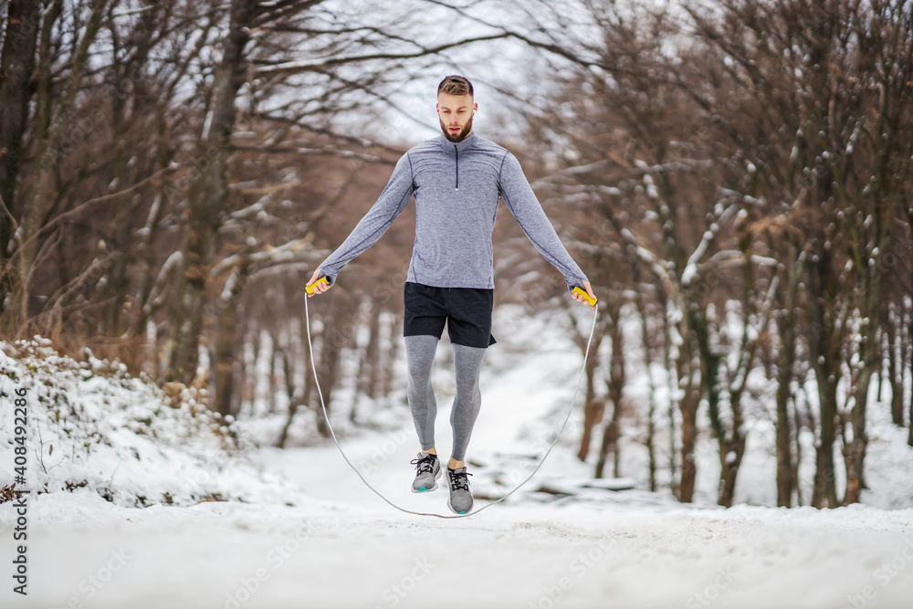 Sportsman in shape jumping rope in nature on snow at winter. Winter fitness, healthy habits, chilly weather