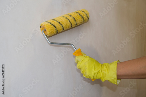 applying a transparent primer to the wall. worker's hand in a yellow glove.