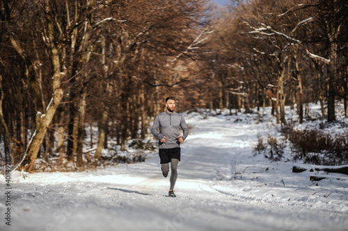 Sportsman jogging in forest at snowy winter day. Winter fitness, sporty lifestyle, healthy life