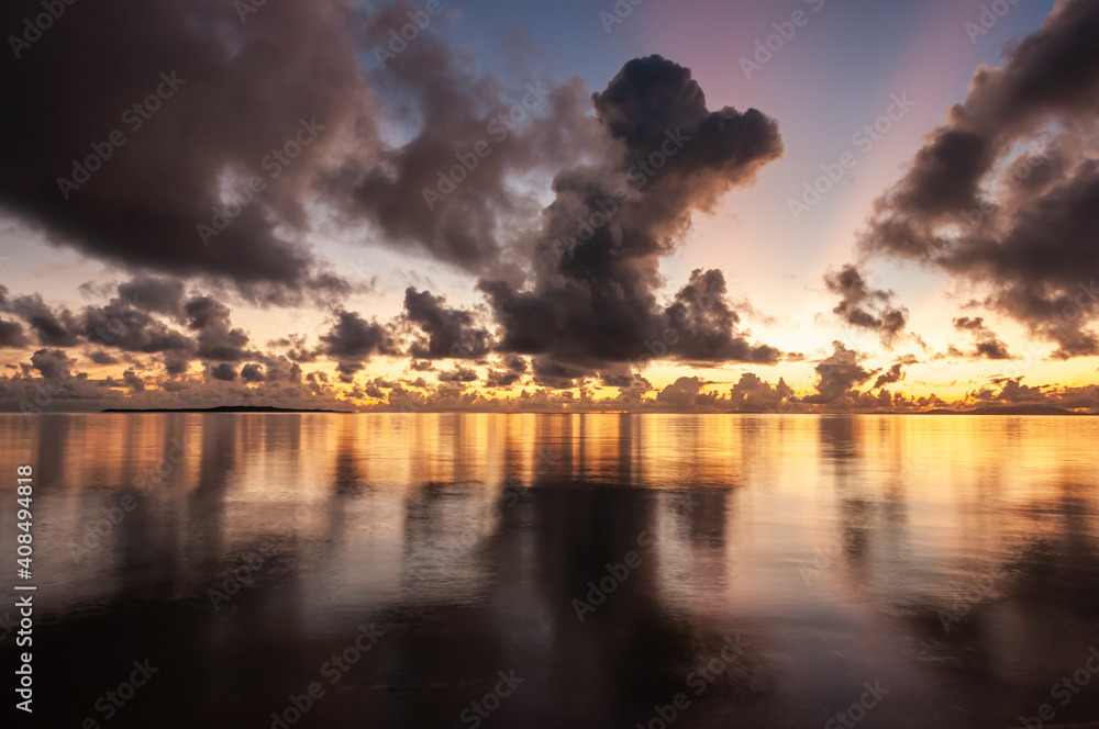 Breathtaking dawn on seashore, colorful sky, dark clouds reflecting on the smooth sea. Iriomote Island.