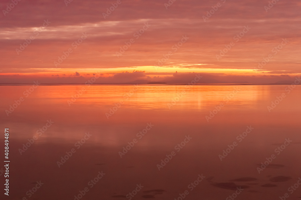 Long exposure of a radiant sunrise with a pink yellow colors reflected in the smooth surface of ocean at Nakano beach. Iriomote island.