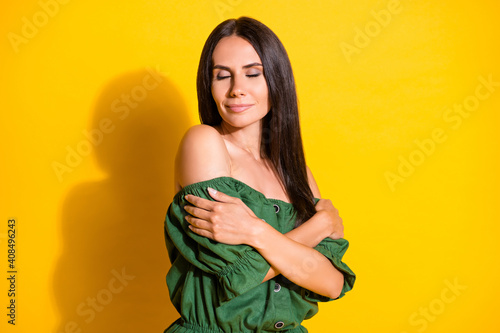 Photo portrait of beautiful brunette embracing herself sensual in green clothes isolated on vibrant yellow color background
