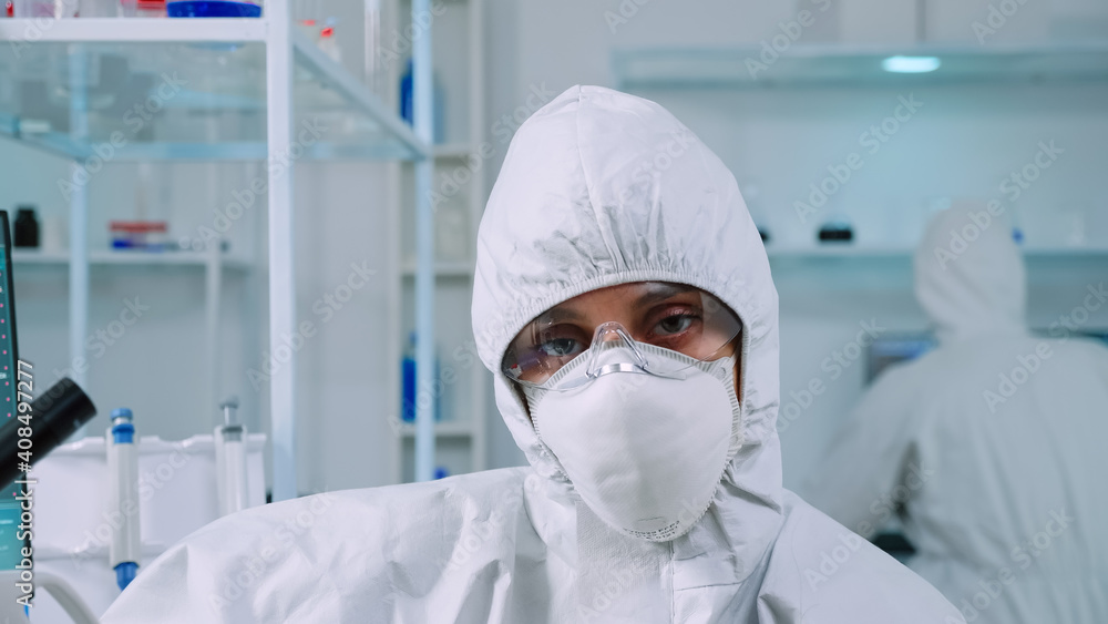 Portrait of tired scientist in coverall looking at camera sitting in modern equipped laboratory. Team of doctors examining virus evolution using high tech and chemistry tools for vaccine development. Portrait of tired scientist in coverall looking at camera sitting in modern equipped laboratory. Team of doctors examining virus evolution using high tech and chemistry tools for vaccine development.