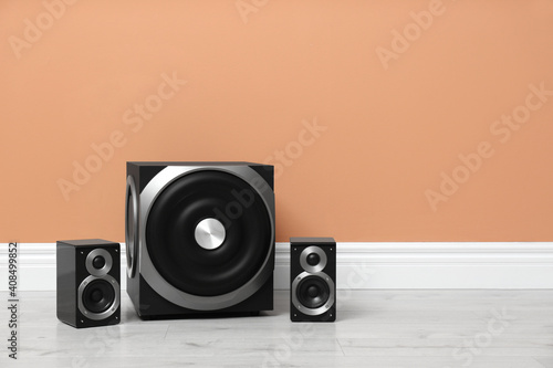 Modern powerful audio speaker system on floor near orange wall. Space for text photo