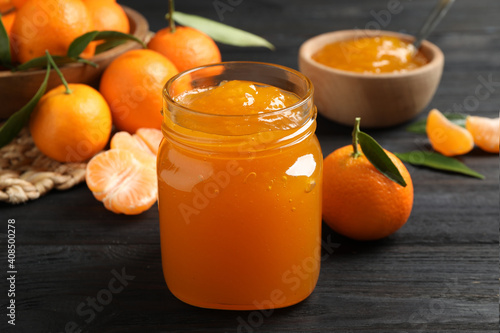 Tasty tangerine jam in glass jar on dark wooden table