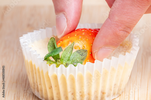 Selective focus closeup of a hand putting a fresh strawberry on a cheesecake on the wooden table photo