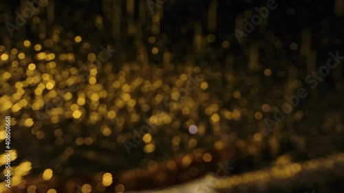 On blurred bokeh background camera focuses on electric guitar lying in rain. Instrument on surface of water, covered in splashes of water, glitters in yellow neon light. Close up. Slow motion.