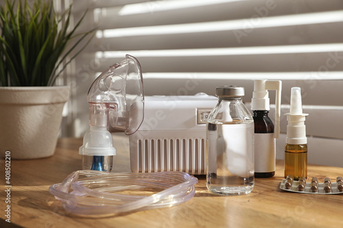 Modern nebulizer with face mask and medications on wooden table indoors. Inhalation equipment